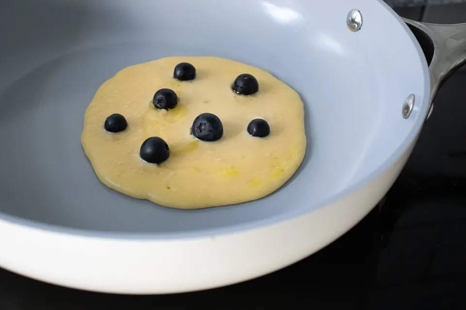 Blueberry pancake cooking in a gray nonstick skillet
