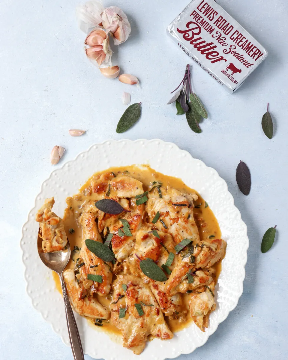 Creamy chicken on white plate with garlic, sage, and butter