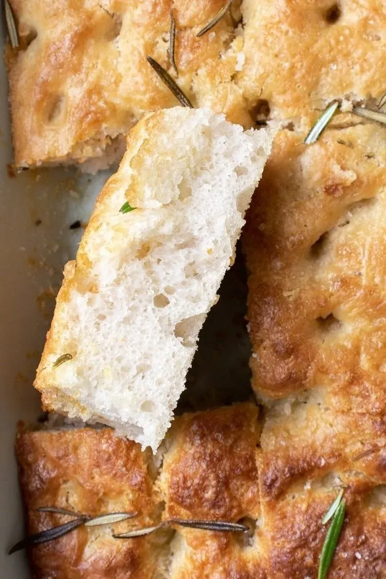 Torn piece of golden sourdough focaccia with rosemary sprigs