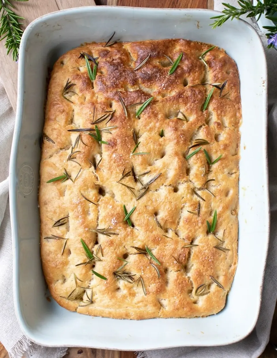 Golden sourdough focaccia in baking dish topped with rosemary