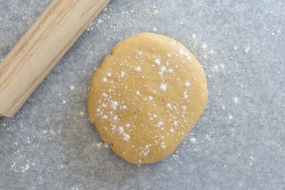 Rolled pie dough dusted with flour beside a wooden rolling pin