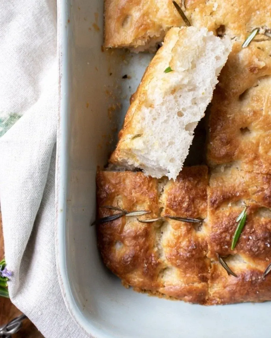 Slice of sourdough focaccia lifted from rosemary-topped golden bread