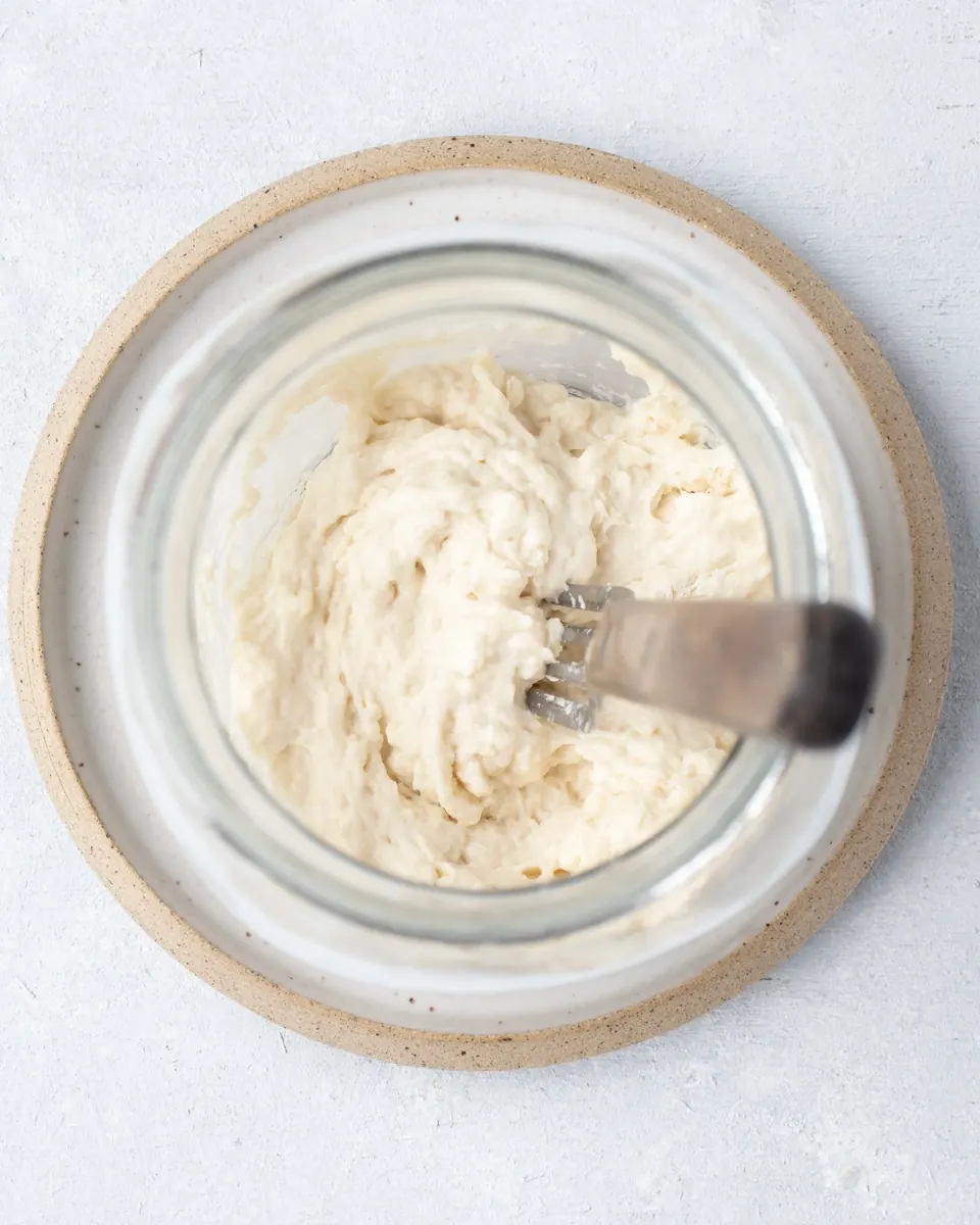 Sourdough starter being stirred in a glass jar
