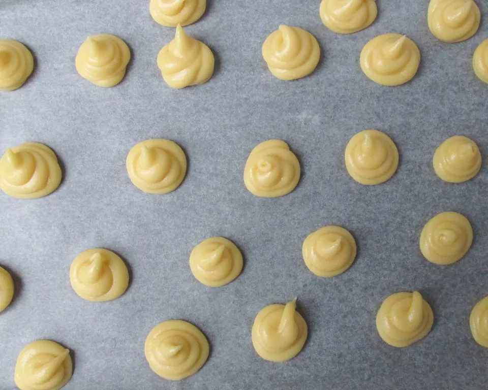 Piped profiterole pastry rounds on a parchment-lined baking sheet