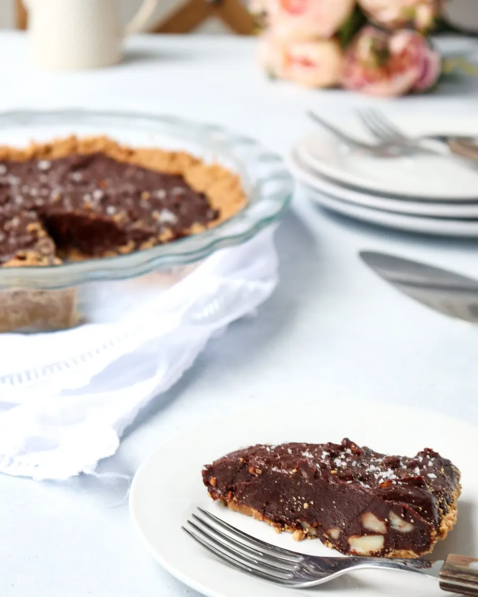 Slice of chocolate macadamia pie on plate beside whole pie