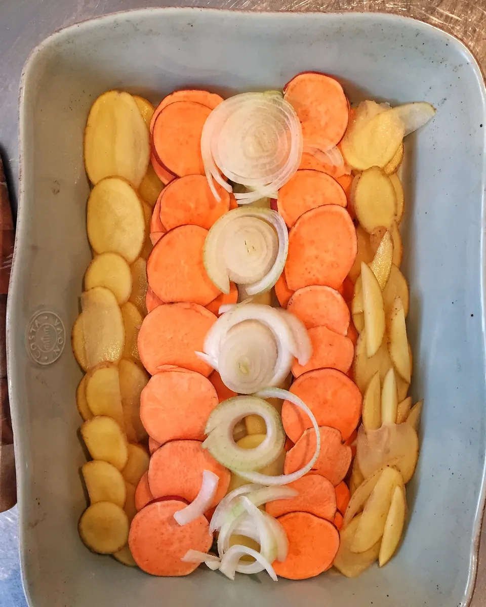 Layered potato and sweet potato gratin with sliced onions in baking dish