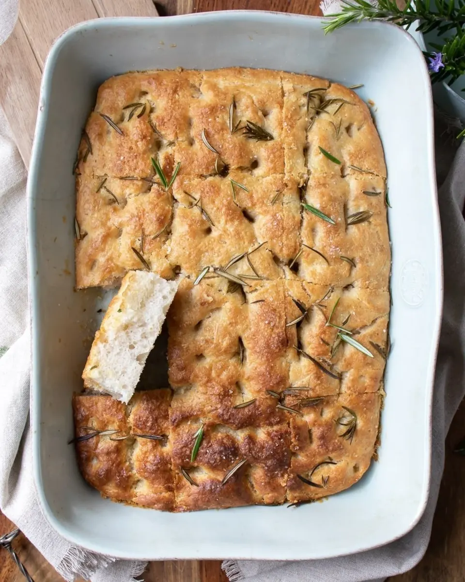 Golden rosemary sourdough focaccia in baking dish with piece removed