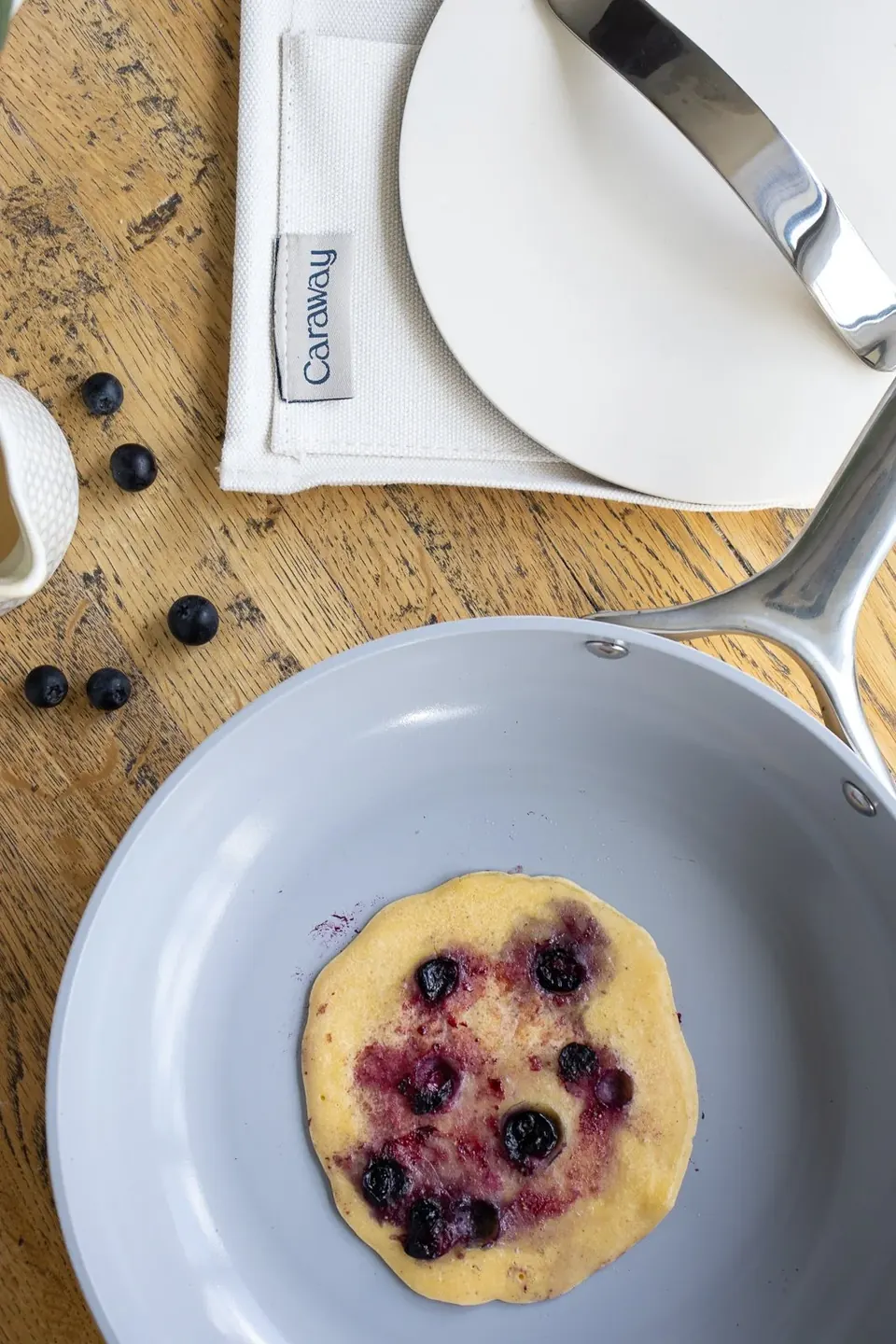 Blueberry pancake cooking in gray Caraway nonstick skillet on wooden table