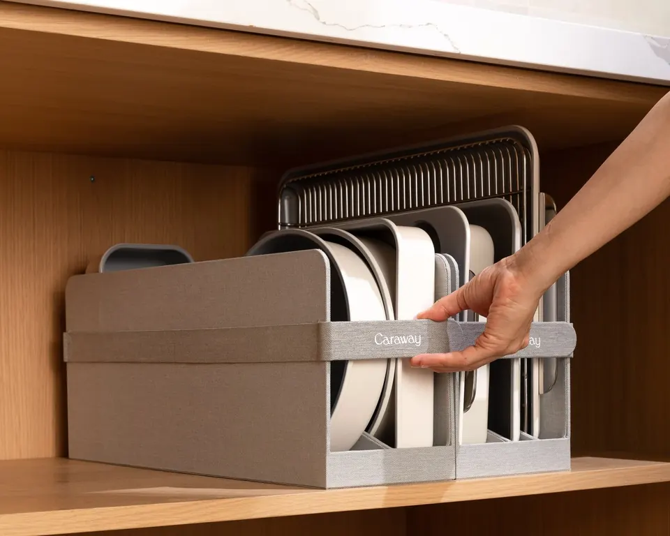 Hand organizing Caraway bakeware set in wooden kitchen cabinet