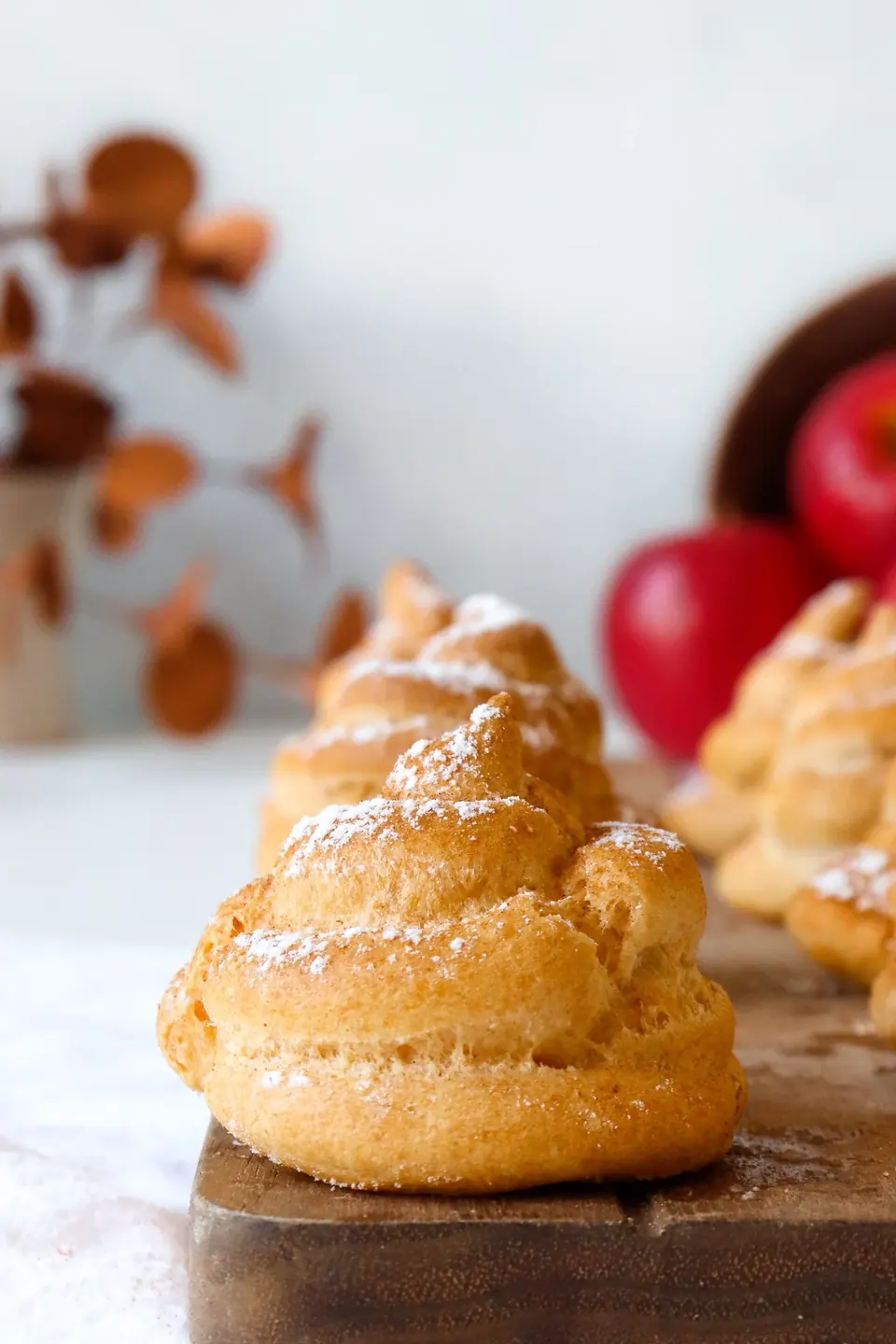 Powdered sugar-dusted profiteroles on a wooden board with red apples