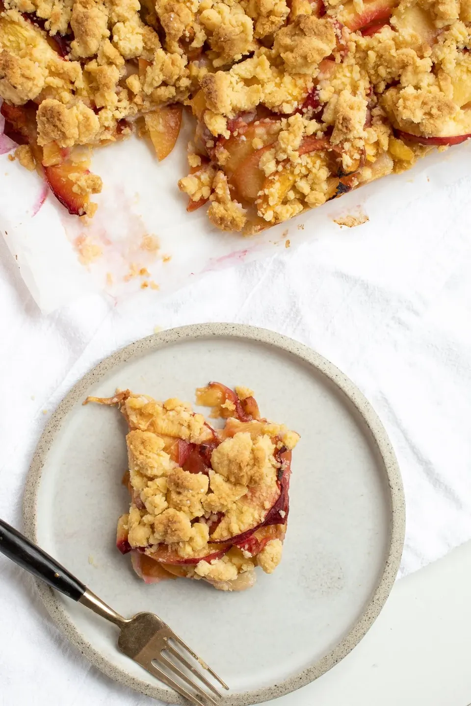 Peach crumble bar square on plate with baking dish