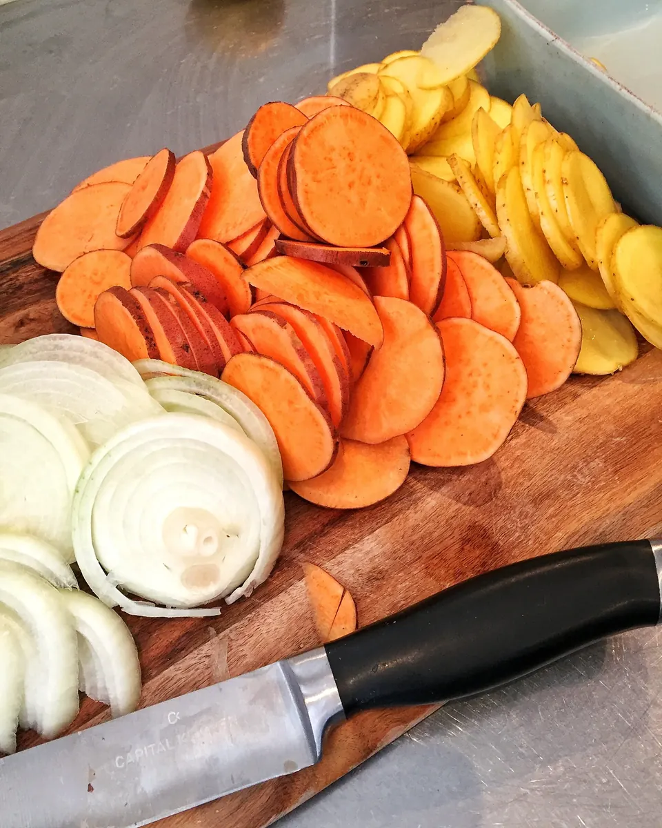 Sliced potatoes, sweet potatoes, and onions on a cutting board