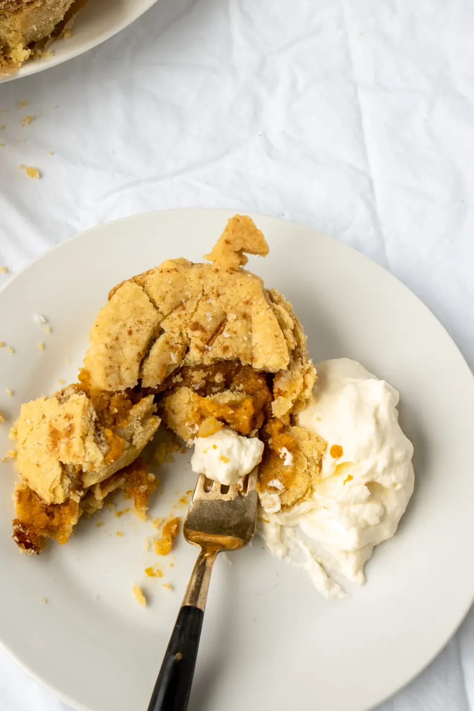 Broken mini pumpkin pie with whipped cream on white plate
