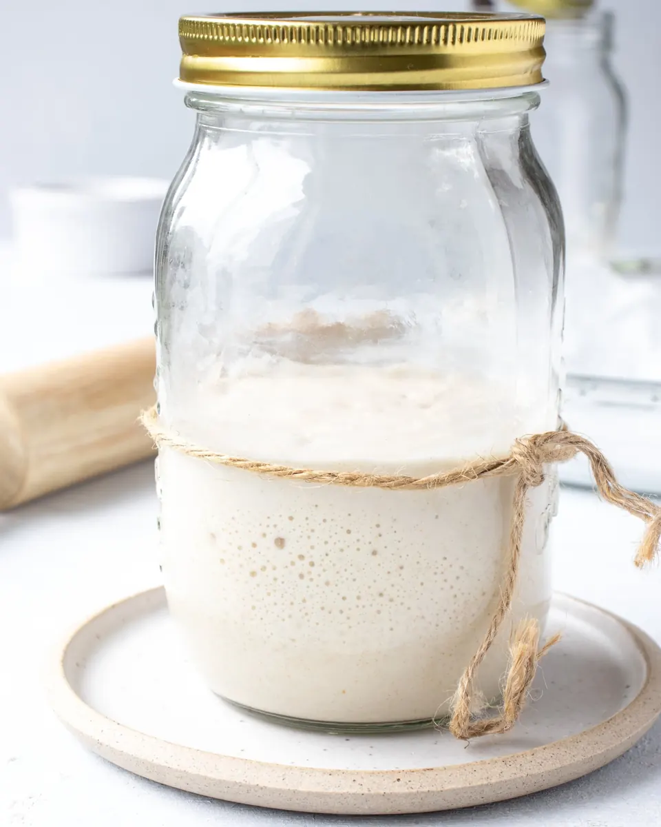 Jar of bubbly sourdough starter tied with twine on plate