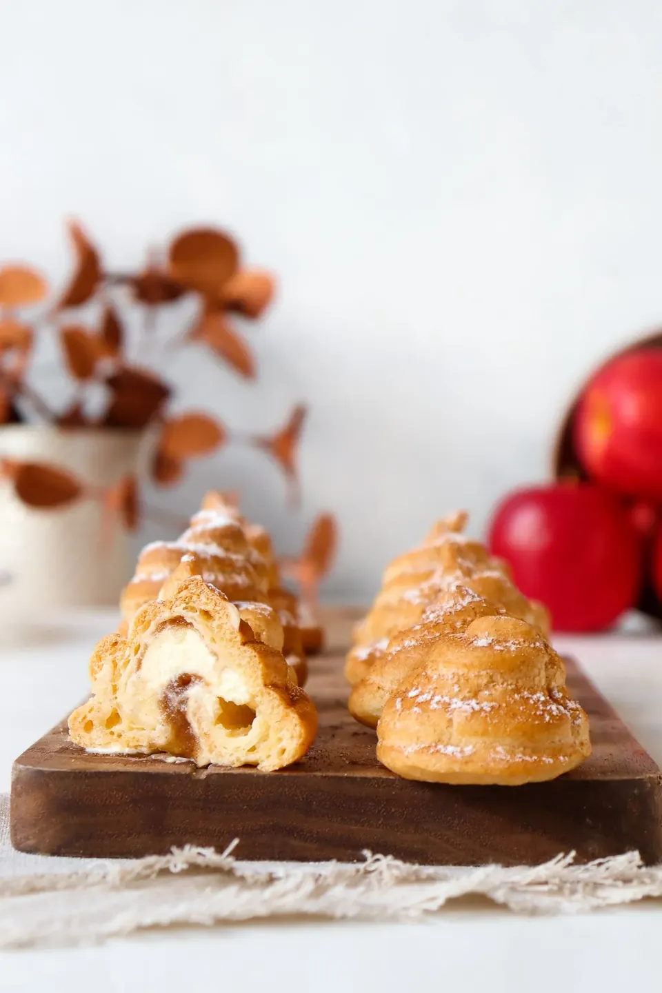 Apple-spiced profiteroles dusted with powdered sugar on wooden board